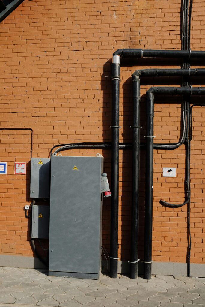 Outdoor scene showing electrical pipes and power box mounted on a brick wall.